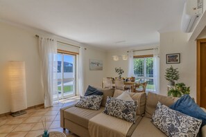 Ein Wohnzimmer mit Sofa, gemusterten Kissen, einem Esstisch mit Stühlen und Blick durch Glastüren.