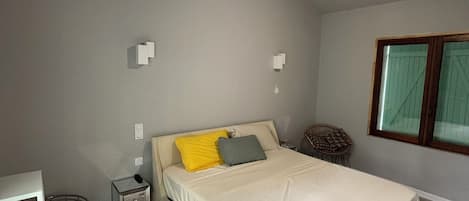 A bedroom with a bed, bedside tables, a small round table, a chair, and a window with curtains.