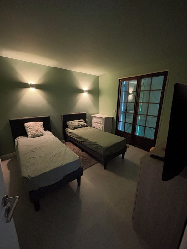 A bedroom with two beds, a nightstand, a dresser, and a sliding glass door.