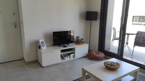 Uma sala de estar moderna com uma televisão de tela plana sobre um armário branco, uma mesinha com uma tigela e um abajur.