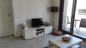 Ein modernes Wohnzimmer mit einem Flachbildfernseher auf einem weißen Schrank, einem kleinen Tisch mit einer Schale und einer Stehlampe.