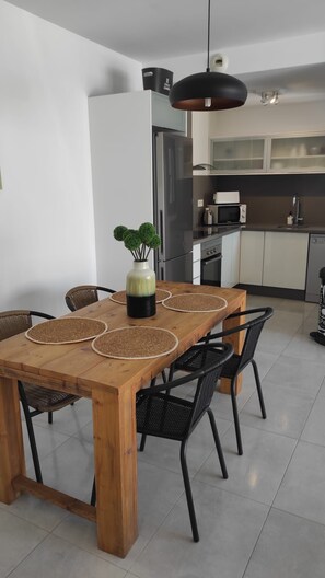 Uma área de refeições com uma mesa de madeira, jogos americanos trançados, cadeiras pretas e um vaso com planta.
