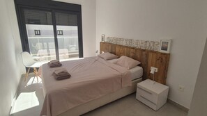 Quarto com cama, mesas de cabeceira, uma cadeira e janela.