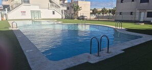 Piscina com água azul cristalina, rodeada por grama sintética e bordas de concreto.