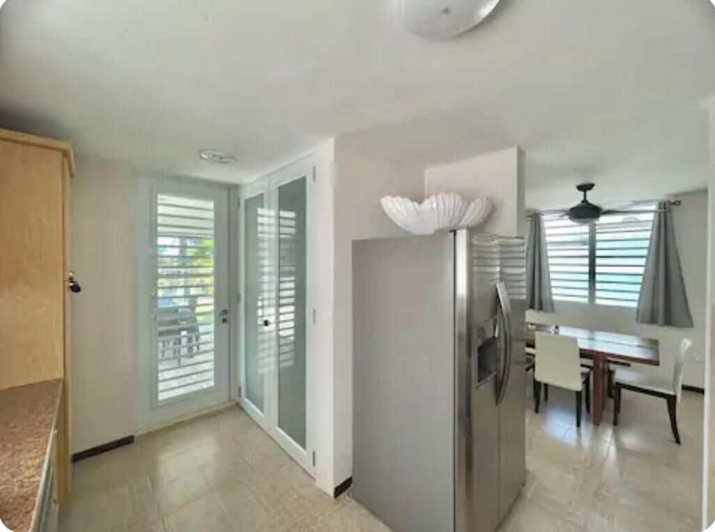 A modern kitchen with a refrigerator, a dining table with chairs, and a ceiling fan.