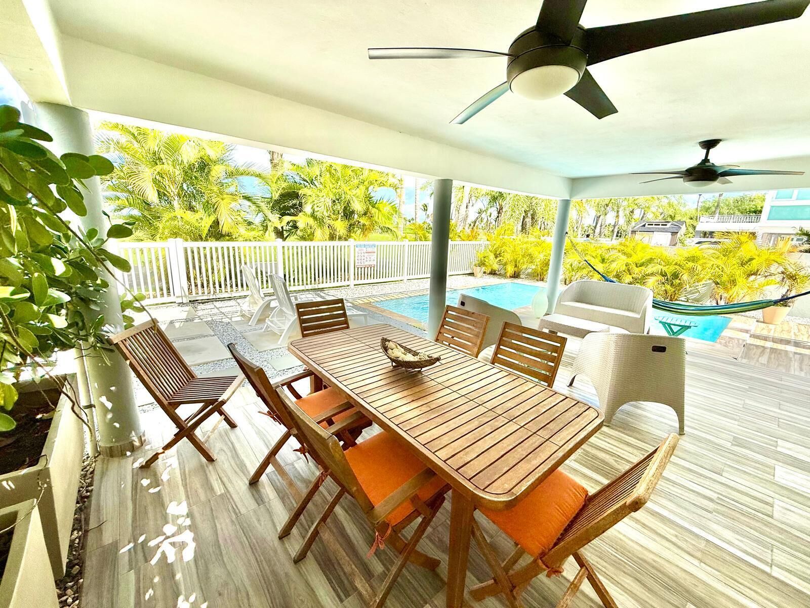 An outdoor patio with a pool, wooden furniture, and ceiling fans.