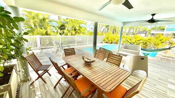 An outdoor patio with a pool, wooden furniture, and ceiling fans.
