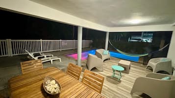 Un patio al aire libre con piscina, mobiliario de madera y cerca blanca.