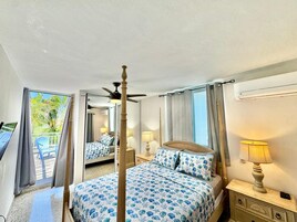 Un dormitorio con cama con dosel, ventilador de techo y balcón con vista a palmeras.