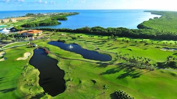 Campo de golf con varios obstáculos de agua, un club de campo y vistas al océano.