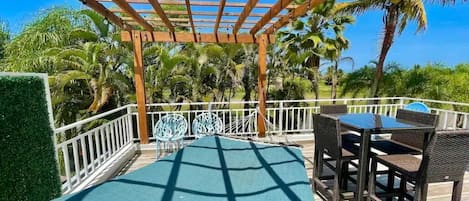 Un espacio al aire libre techado con piscina, mobiliario y vistas a palmeras.