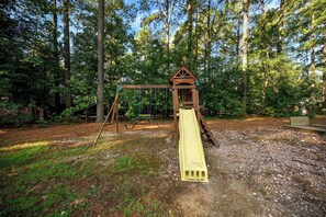 A wooden swing set in a wooded area with a slide. - Over Yonder Inn | Hot Tub, Firepit & Pool Table (Broken Bow)