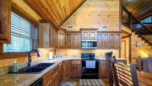 A wooden cabin interior with a kitchen, dining area, and staircase. - Over Yonder Inn | Hot Tub, Firepit & Pool Table (Broken Bow)