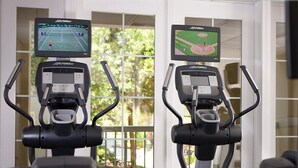 Two exercise bikes with screens displaying sports games, positioned in a room with a view of a balcony. - 2 Bedroom Villa Harbour Club Resort w/ Amenities (Hilton Head Island)