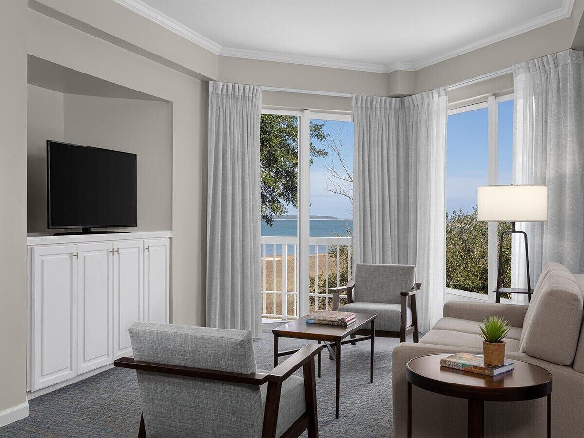 A hotel room with a television, seating area, and a view of the sea.