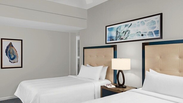 A hotel room with two beds, a ceiling fan, a framed artwork, and a nightstand with a lamp. - 2 Bedroom Villa Harbour Club Resort w/ Amenities (Hilton Head Island)