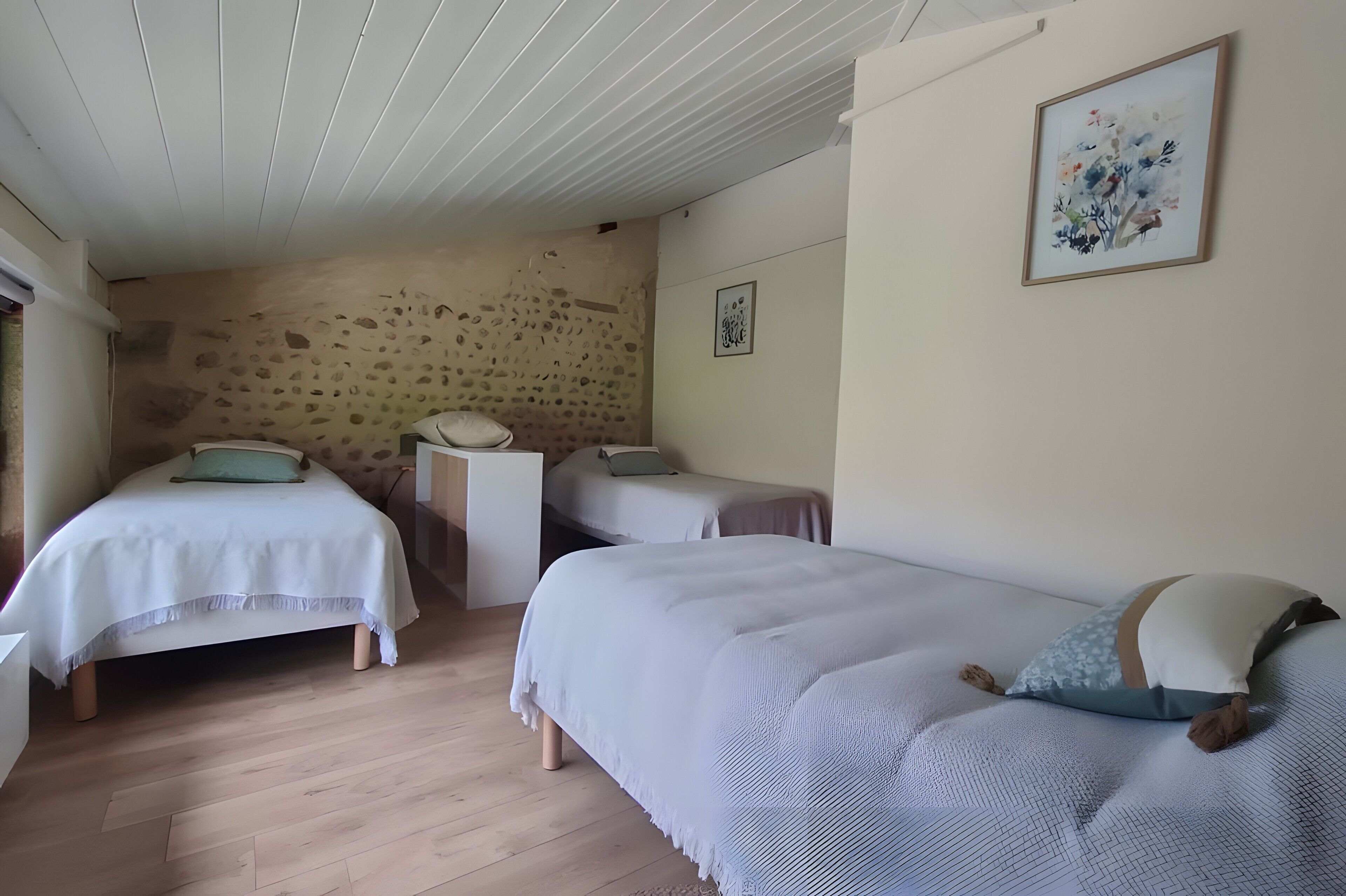 A bedroom with two single beds, a small bedside table, a wall-mounted artwork, and a stone wall.