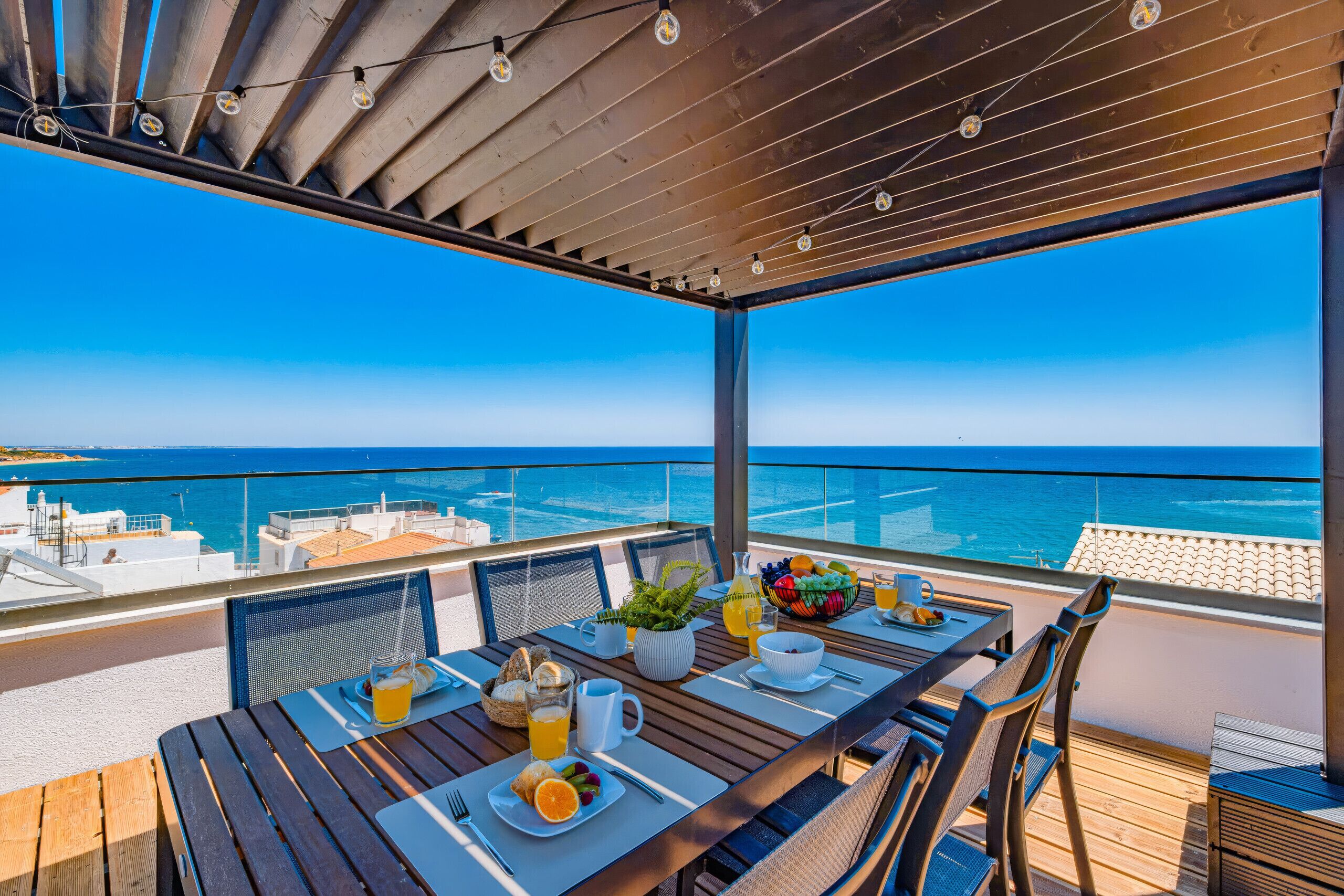 Een zonnig buitendiner met uitzicht op zee, met een gedekte tafel voor het ontbijt en een pergola erboven.