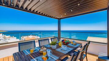 Een zonnig buitendiner met uitzicht op zee, met een gedekte tafel voor het ontbijt en een pergola erboven.
