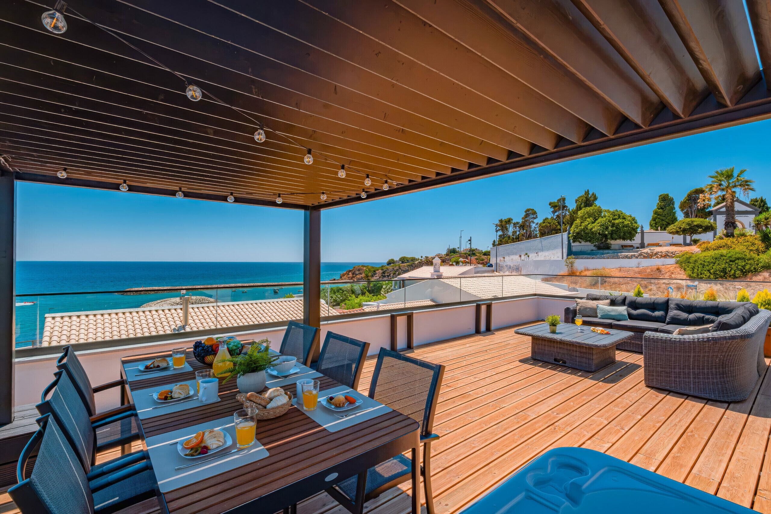 Un espace extérieur abrité, aménagé pour les repas, avec vue sur la mer, du mobilier en bois et une table dressée avec de la nourriture et des boissons.