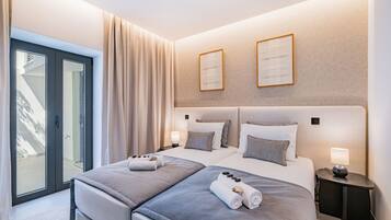 A modern hotel room with a large bed, two bedside tables, and a sliding glass door leading to a balcony.