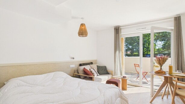 Een moderne hotelkamer met een groot bed, een bank, een eettafel en uitzicht op het groen.
