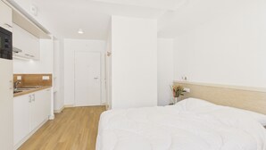 Een hotelkamer met een bed, een klein nachtkastje, een wandlamp en uitzicht op de keuken.