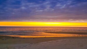 Een strand bij zonsondergang, met een zandstrand en enkele mensen.