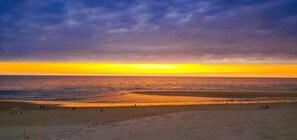 Ein Strand bei Sonnenuntergang, mit sandigem Ufer und einigen Personen.