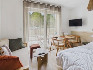 A hotel room with a bed, a small table with two chairs, a TV mounted on the wall, and a view of the outdoors through the window.