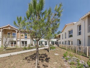 Ein Wohngebäude mit einem zentralen Baum, einem umzäunten Innenhof und einem Weg.