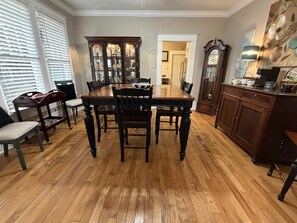 A dining room with a wooden table and chairs, a cabinet with a clock, and a window with blinds. - Anchored in Paradise, Walk to Beach & Island View Casino (Gulfport)