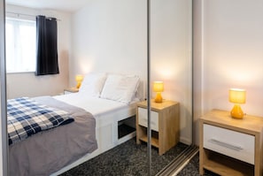 Ein Schlafzimmer mit einem Bett, Nachttischen, einem Spiegel und einem Fenster mit Vorhängen.