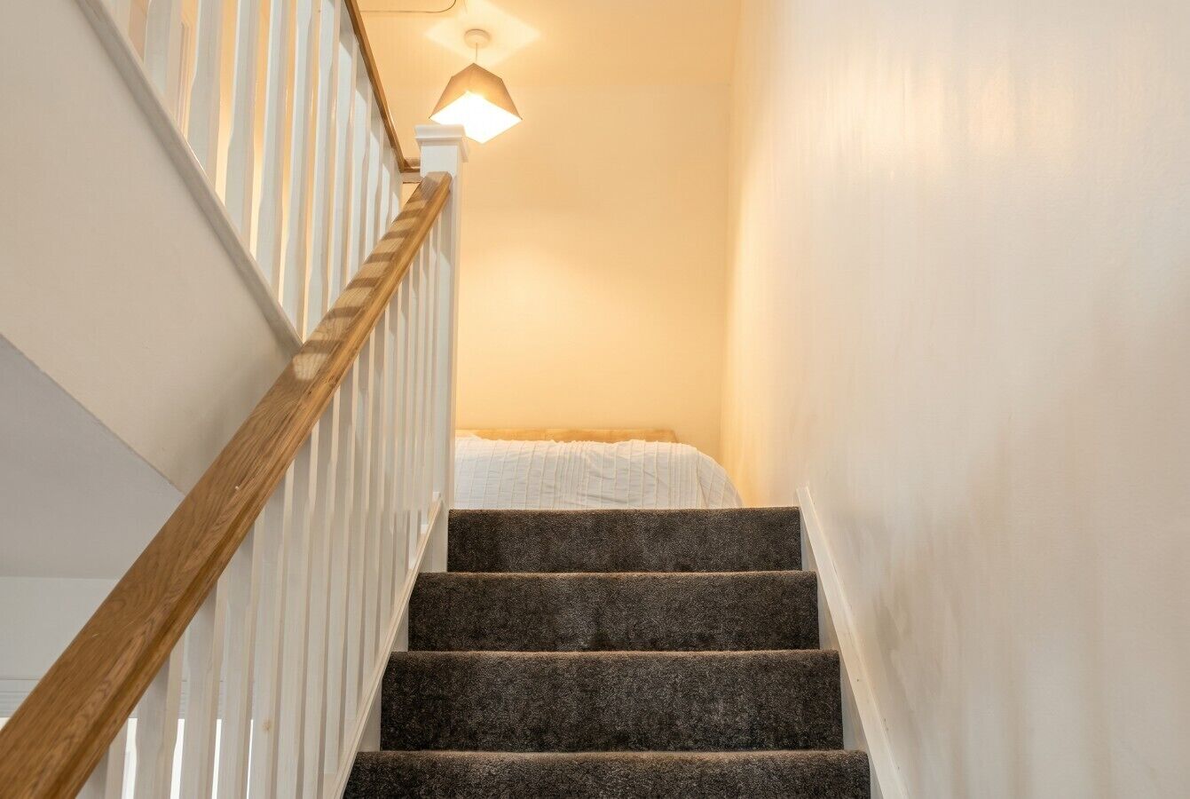 A staircase with wooden handrails and carpeted steps leading to a room with a bed.