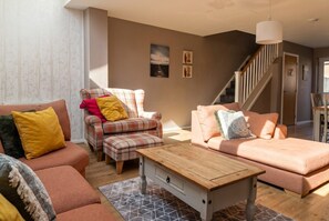 A living room with a sofa, armchair, and ottoman, a wooden coffee table, and a staircase leading to another room. - Pet-Friendly 3-Bed Home · Sleeps 6 · Free Parking in Salford (Greater Manchester)