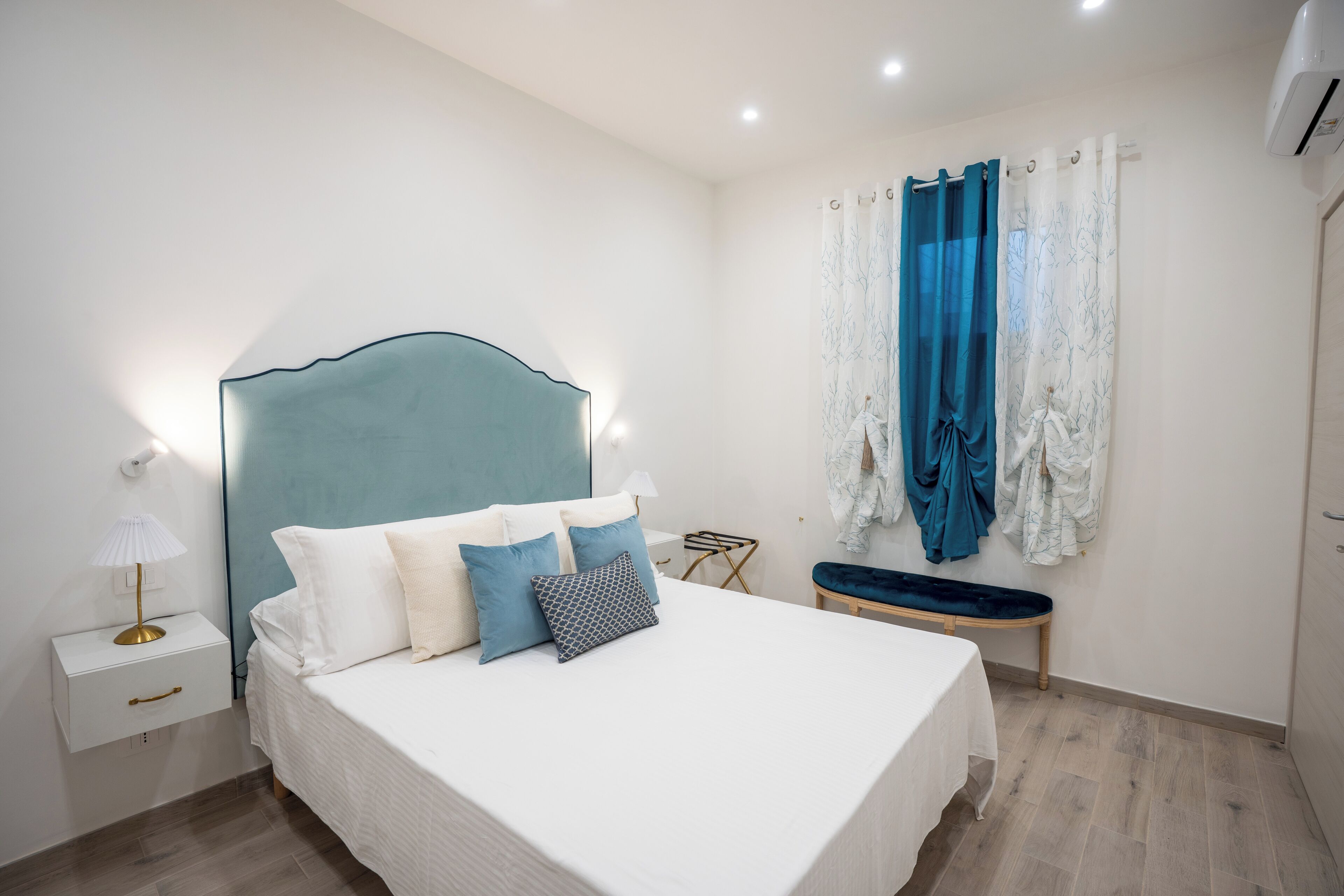 Un dormitorio con cama, mesita de noche, lámpara y una ventana con cortinas.