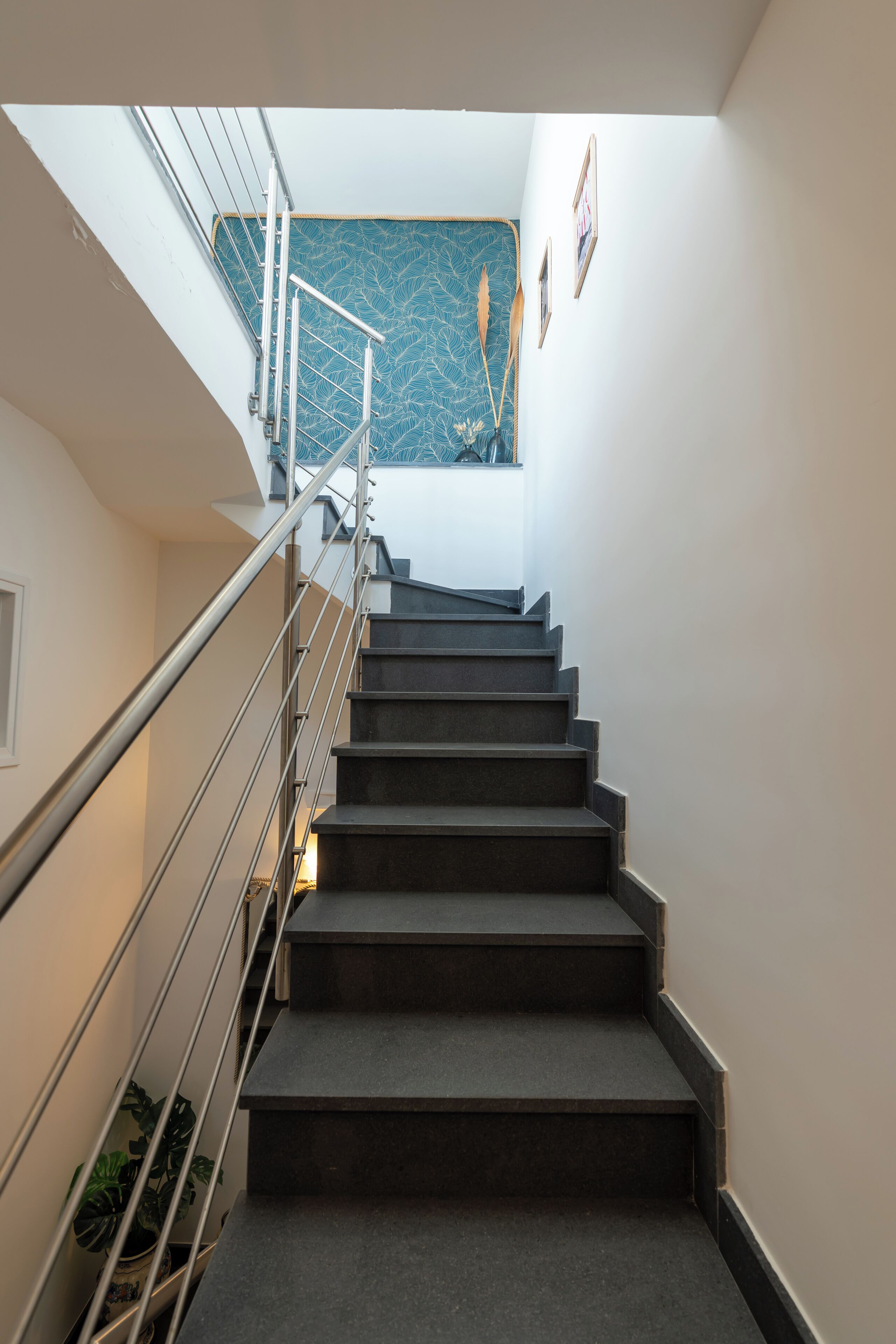 Una escalera con barandillas metálicas y escalones oscuros que lleva a un rellano con pared de diseño azul y fotografías enmarcadas.