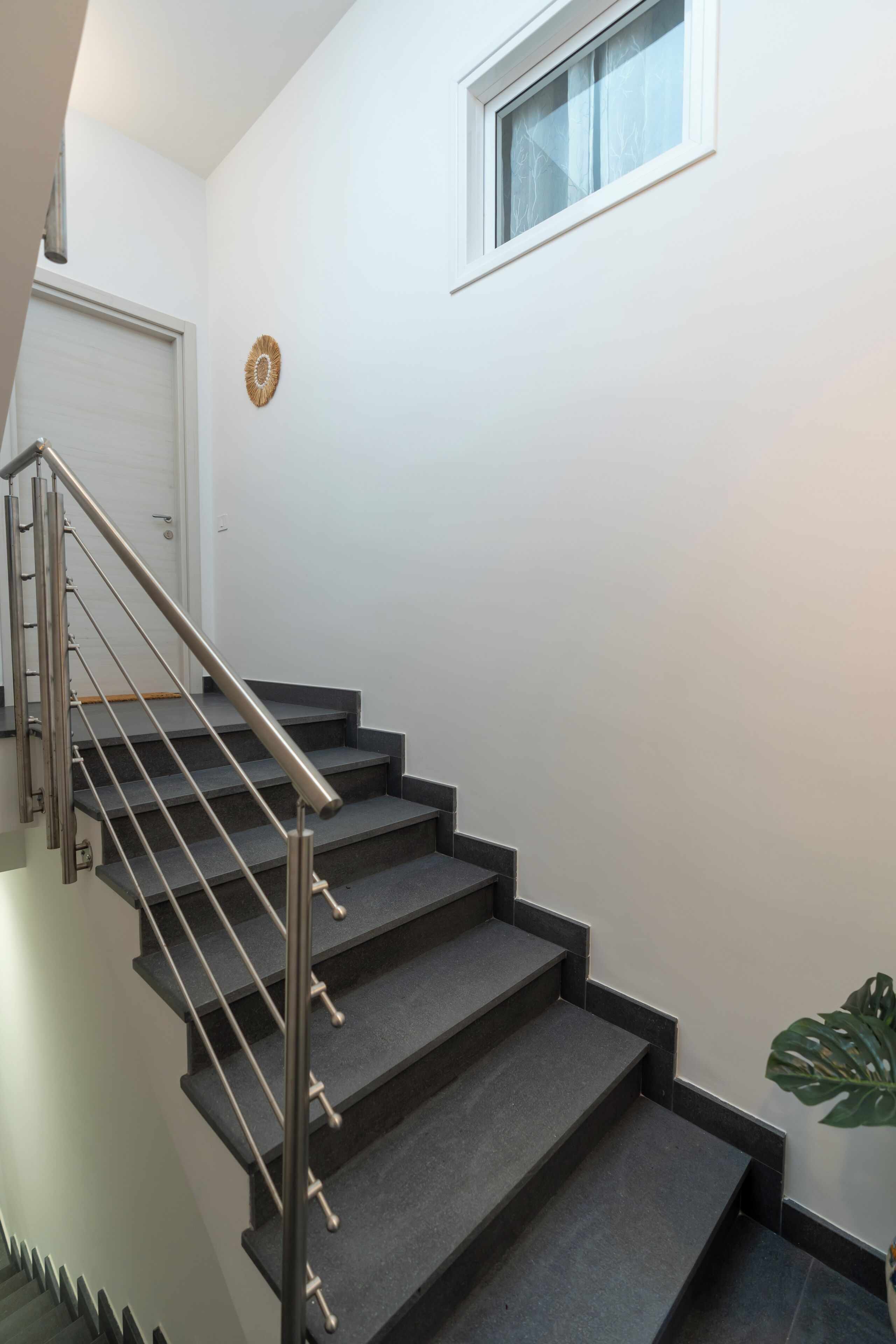 A staircase with a metal handrail and dark steps, leading to a white door.