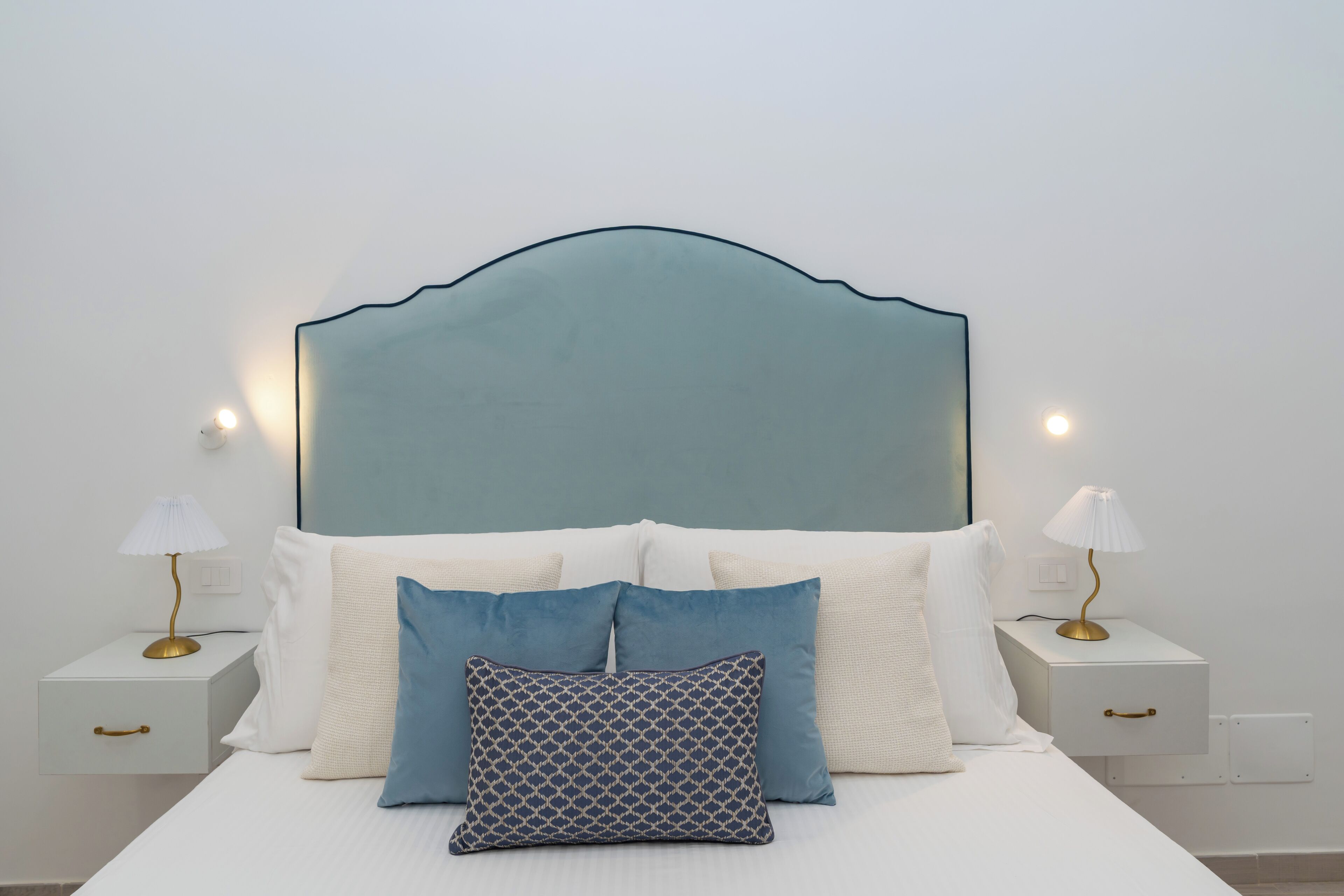A bedroom with a bed, white bedding, two bedside tables with lamps, and a headboard.