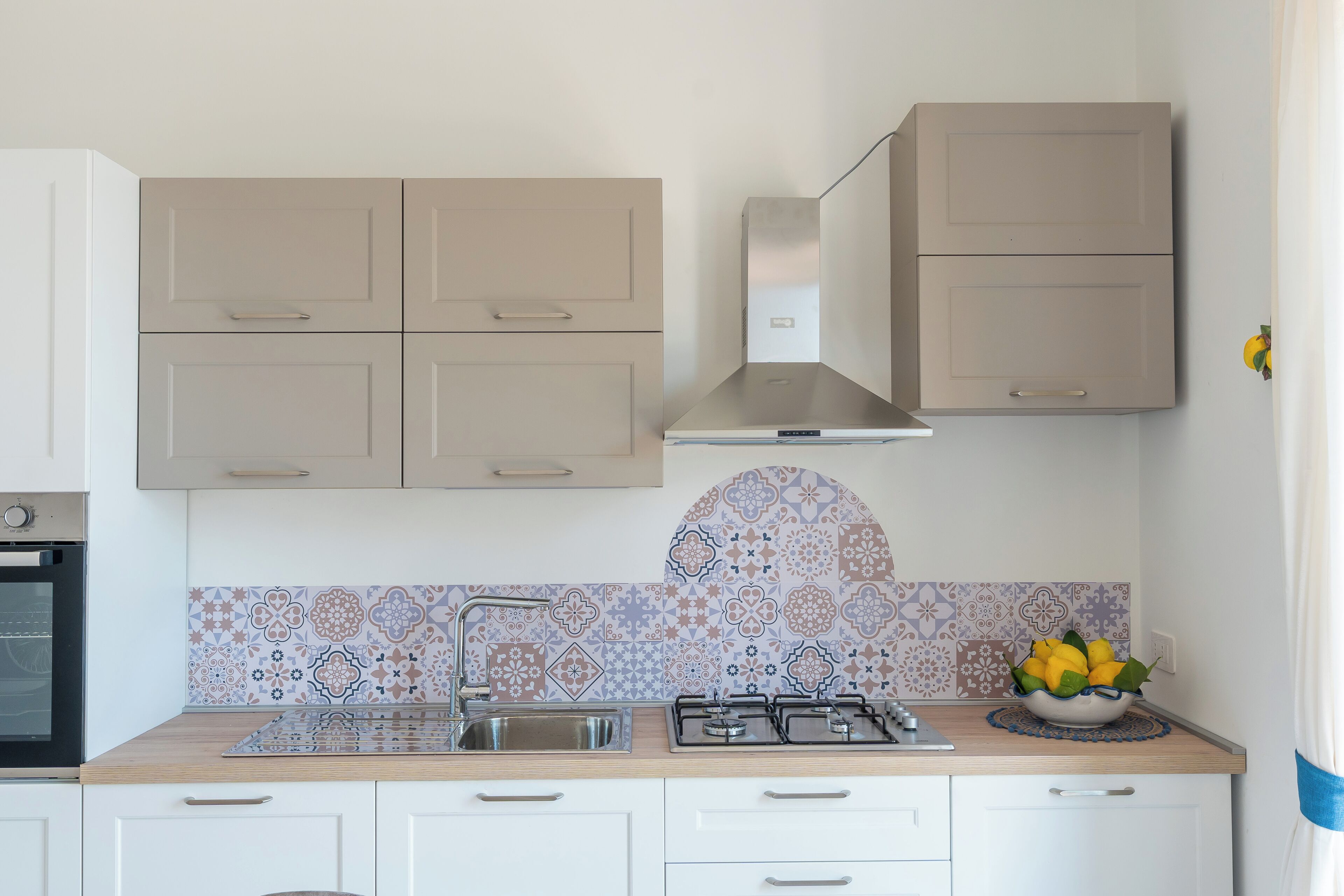 Una cocina con gabinetes blancos, un lavamanos de acero inoxidable, una estufa a gas y un salpicadero decorativo.