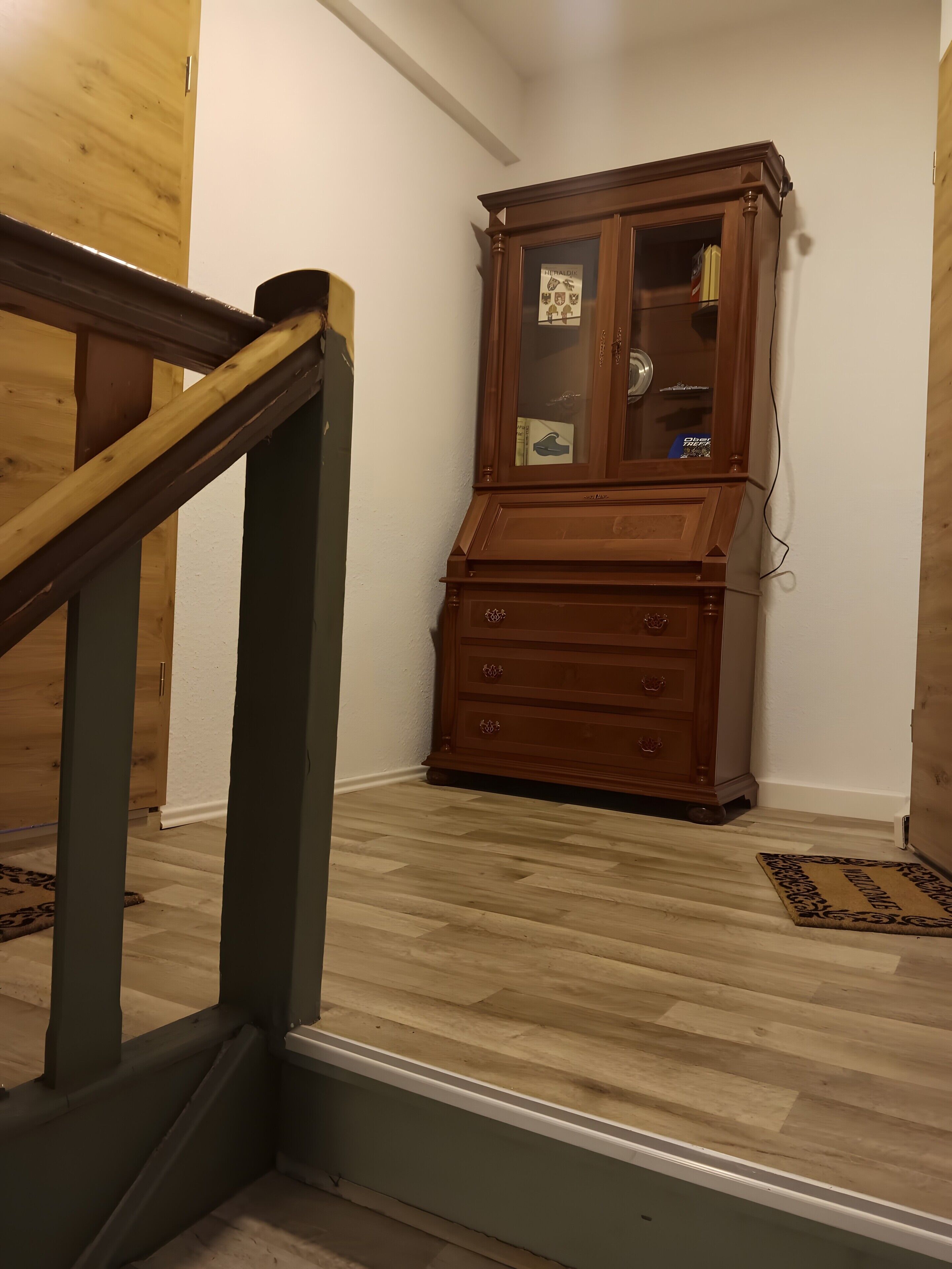 A wooden staircase with a handrail, a wooden cabinet with glass doors, and a patterned rug on the floor.