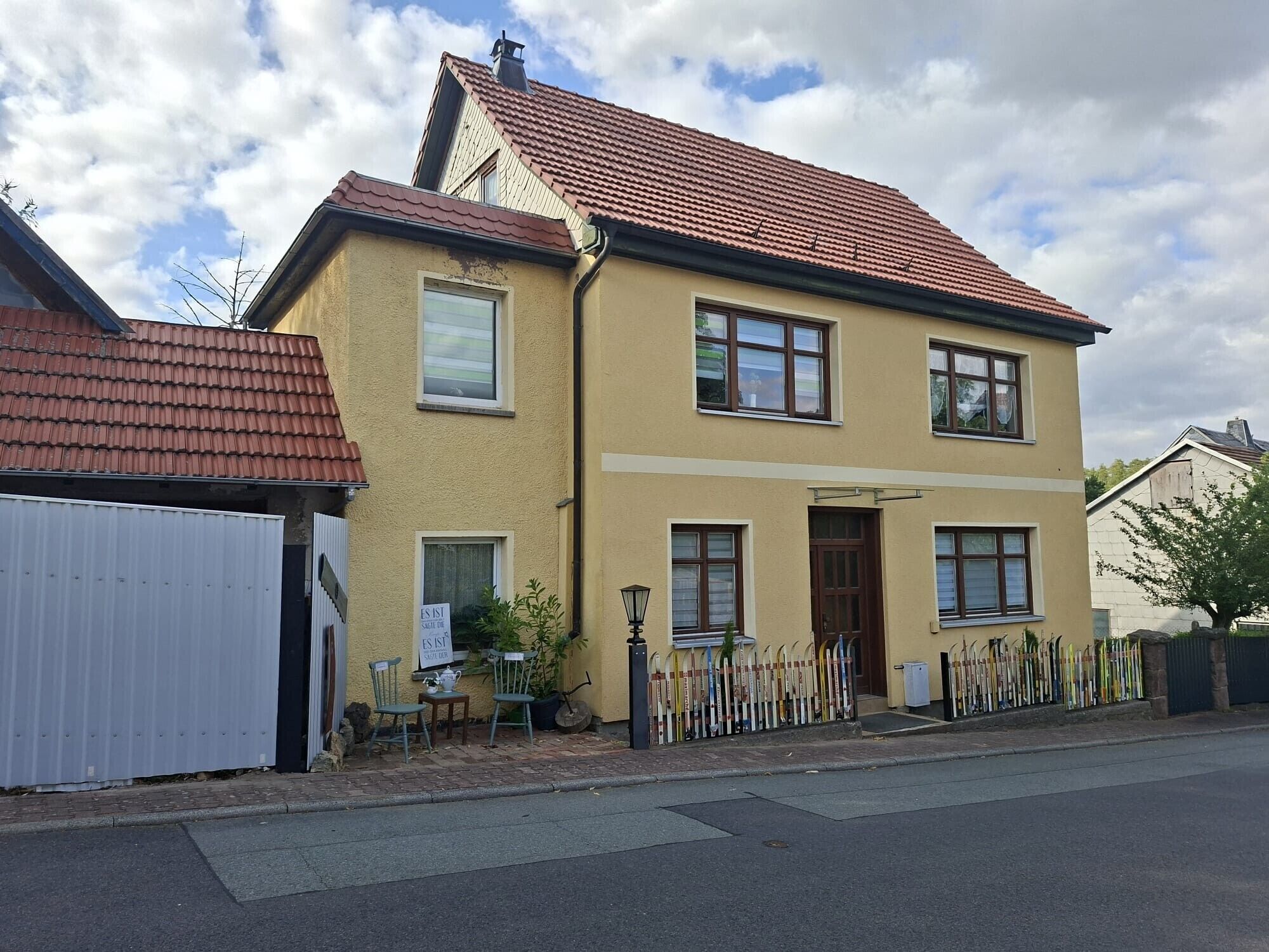Ein zweistöckiges Haus mit rotem Ziegeldach, einer Garage und einem Zaun mit Skiern.