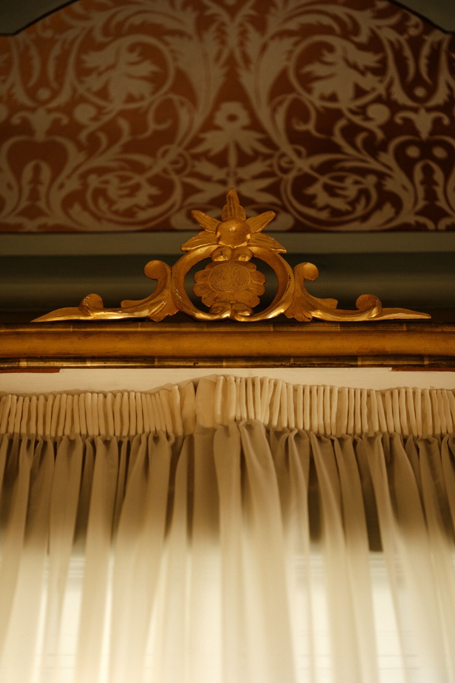 Une pièce avec un papier peint à motifs, un cadre doré décoratif et un rideau drapé.