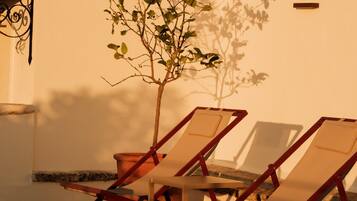 Un patio con dos sillones de descanso, un árbol pequeño y un techo de tejas.