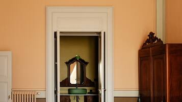 Una habitación con un umbral que da a un baño, un radiador, un armario de madera y un techo con diseño.