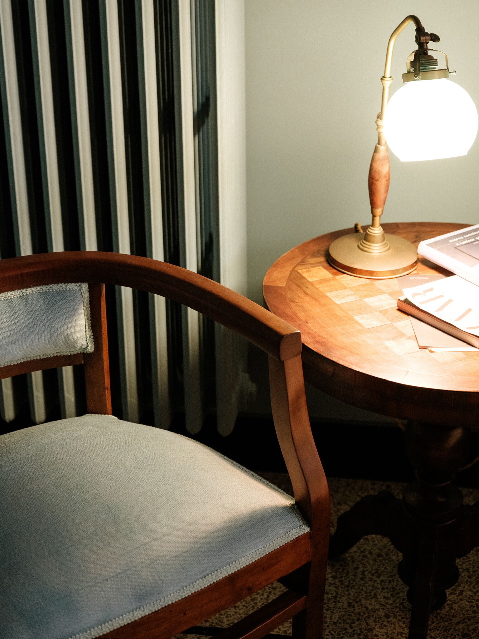 A wooden chair with a cushioned seat and backrest, positioned next to a round wooden table with a lamp.