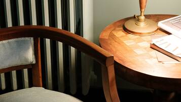 A wooden chair with a cushioned seat and backrest, positioned next to a round wooden table with a lamp.