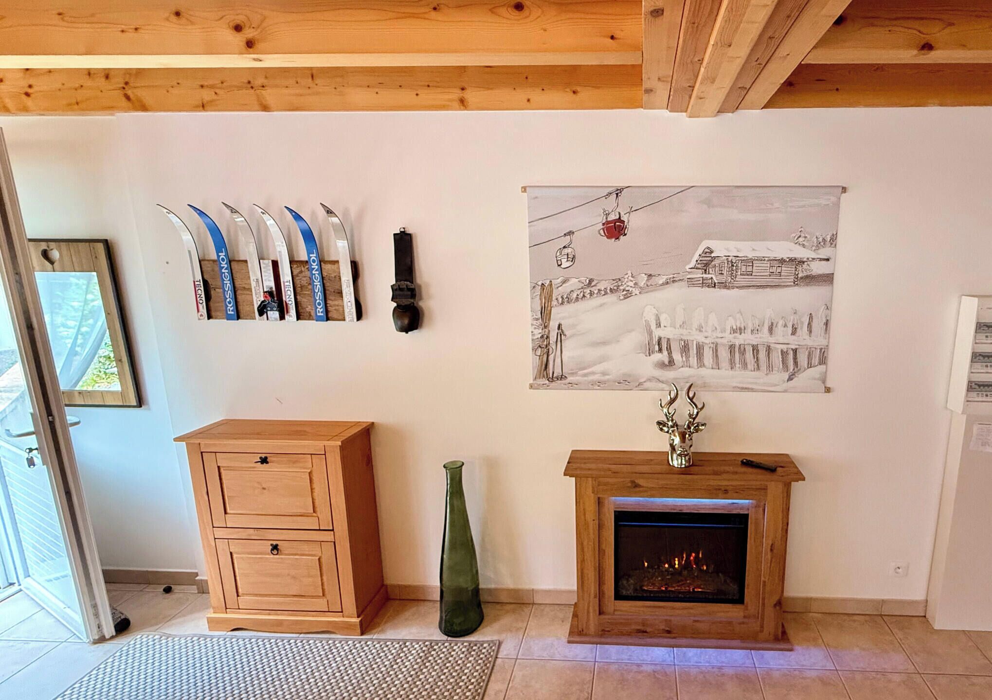 Una sala de estar con chimenea, un armario de madera, un jarrón verde y un soporte para esquíes en la pared.