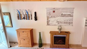 A living room with a fireplace, a wooden cabinet, a green vase, and a wall-mounted ski rack. - La Pergola Le Mont Dore (6 people) (Mont-Dore)