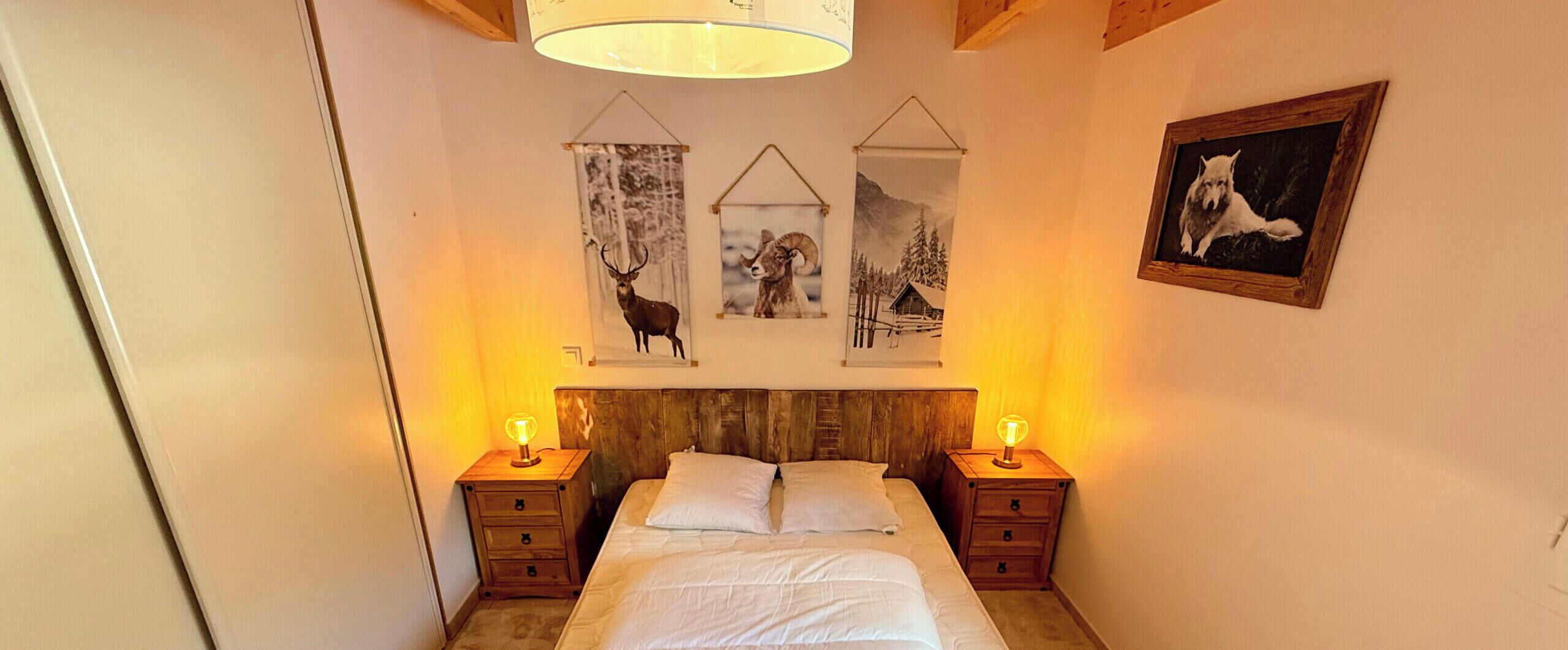 Un dormitorio con cabecera de madera, dos mesitas de noche con lámparas, una cama con ropa de cama blanca y tres cuadros en la pared que representan fauna silvestre.